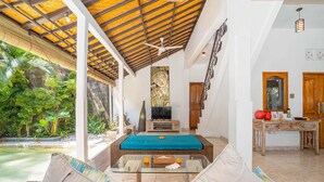 A spacious living area with a glass coffee table, a sofa, a TV, and a wooden cabinet. - Villa Shanti (Seminyak)