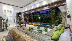 A modern living room with a pool, green cushions, and a glass coffee table. - Villa Kambodja (Seminyak)