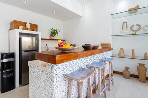 A modern kitchen with a central island, bar stools, a refrigerator, and a water dispenser. - Villa Kambodja (Seminyak)