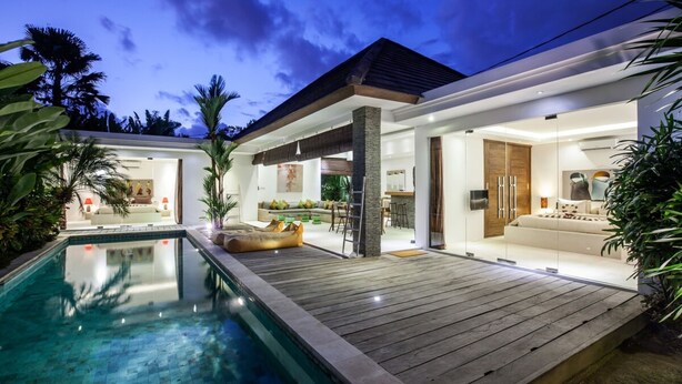A modern house with a swimming pool, wooden deck, and a well-lit interior. - Villa Kambodja (Seminyak)