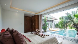 A modern bedroom with a large bed, a view of a swimming pool, and a balcony with plants. - Villa Kambodja (Seminyak)