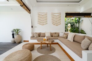 A modern living room with a sectional sofa, a wooden coffee table, and woven poufs.