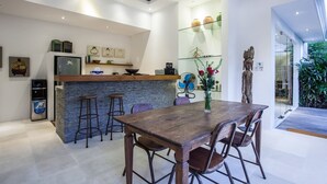 A modern kitchen with a stone island, bar stools, and a dining table with chairs. - Villa Kambodja (Seminyak)