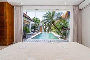 A bedroom with a view of a swimming pool, a wooden wardrobe, and a large bed. - Villa Kambodja (Seminyak)