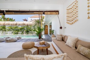 Un salon moderne avec vue sur la piscine, comprenant un canapé, une petite table et un élément décoratif mural.