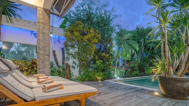 A wooden deck with a lounge area, a swimming pool, and lush greenery. - Villa Laurent (Seminyak)