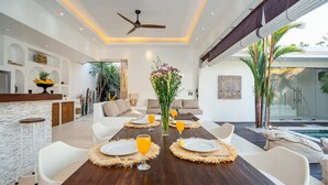 Un espace repas moderne avec une table en bois dressée pour quatre personnes, entourée de chaises blanches.