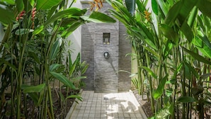 A pathway leading to a stone-walled structure with a small window and a door, surrounded by lush tropical plants. - Villa Suliac (Legian)