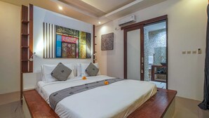 A neatly made bed with a grey bedspread and pillows, a wooden headboard, and a wall-mounted air conditioner. - Villa Athena (Seminyak)