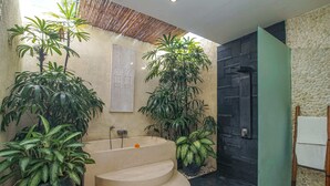 A modern bathroom with a freestanding bathtub, multiple potted plants, and a stone wall. - Villa Athena (Seminyak)