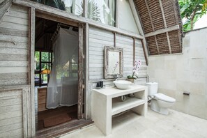A rustic bathroom with a wooden exterior, a white sink, a toilet, and a large mirror. - Villa Bora Bora (Canggu)