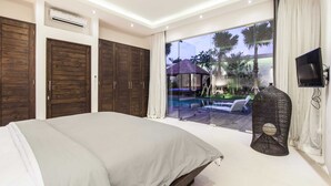 A bedroom with a large bed, wooden wardrobes, a TV, and a view of a pool and palm trees. - Villa Jago (Seminyak)