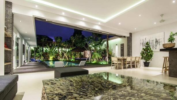 A modern living room with a glass coffee table, a pool, and outdoor seating. - Villa Jago (Seminyak)