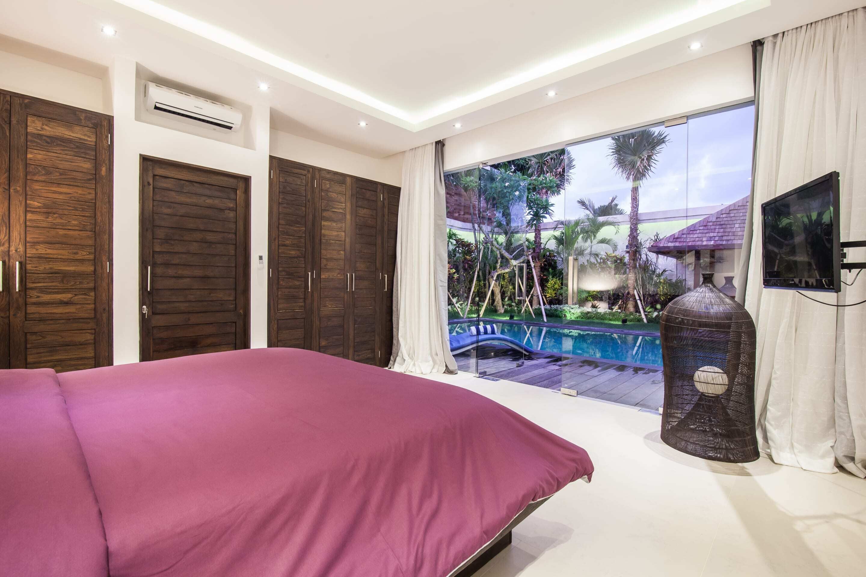 Un dormitorio con una cama grande, armarios de madera, televisor y vistas a una piscina y jardín.