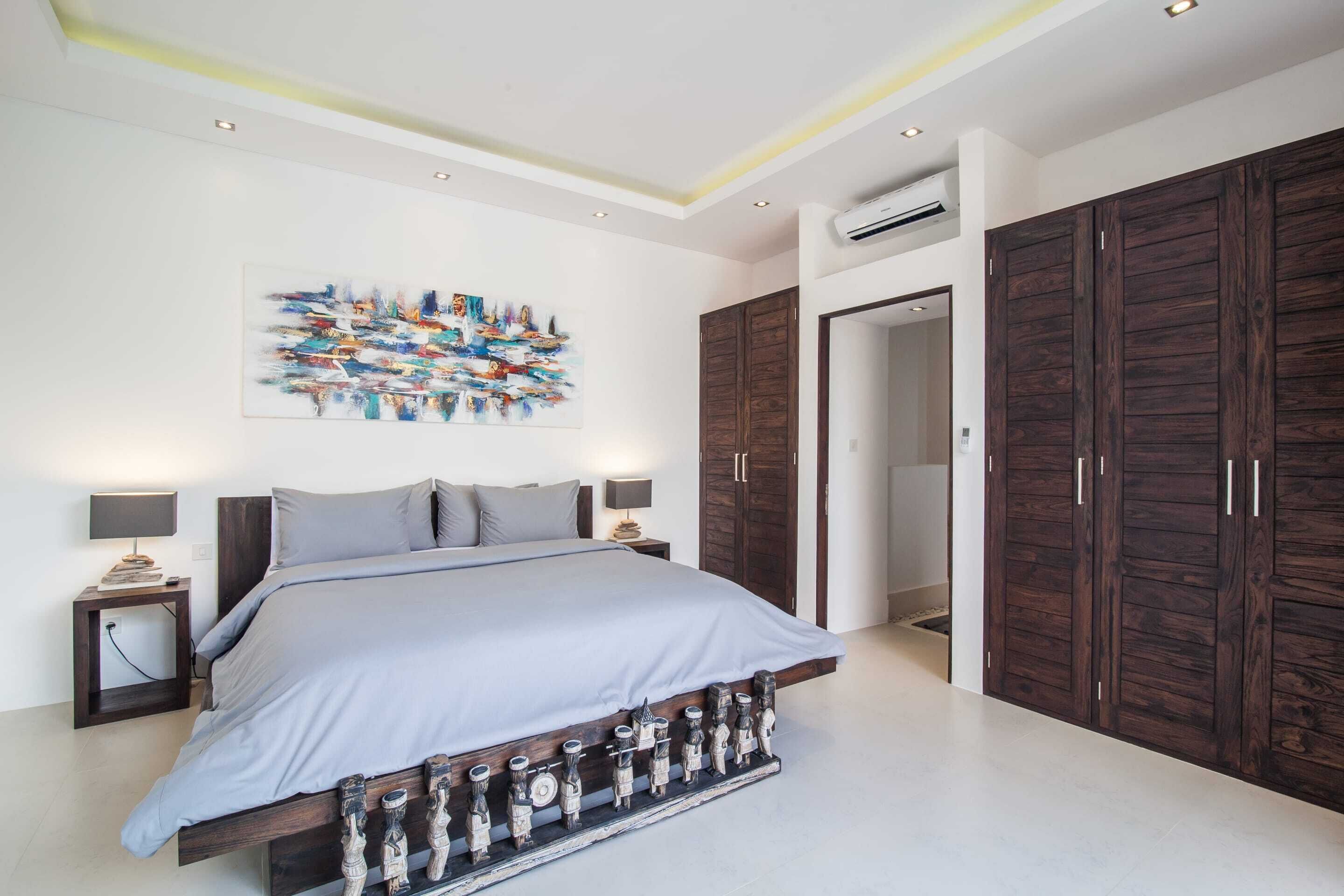 A bedroom with a bed, nightstands, a wall art piece, and wooden wardrobes.