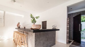 A modern kitchen with a central island, bar stools, a potted plant, and a decorative sculpture. - Villa Jago (Seminyak)