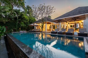 A poolside area with lounge chairs and umbrellas, surrounded by lush greenery. - Villa Bali Sari (Canggu)