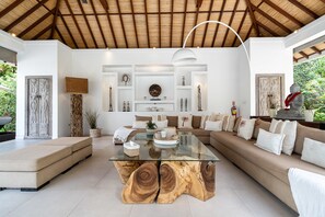 A spacious living area with a glass coffee table, a sofa set, and a ceiling with wooden beams. - Villa Bali Sari (Canggu)