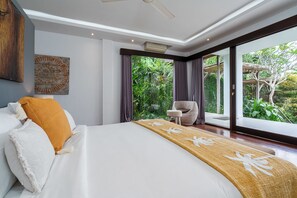 A bedroom with a large bed, a small table, and a view of greenery through the window.