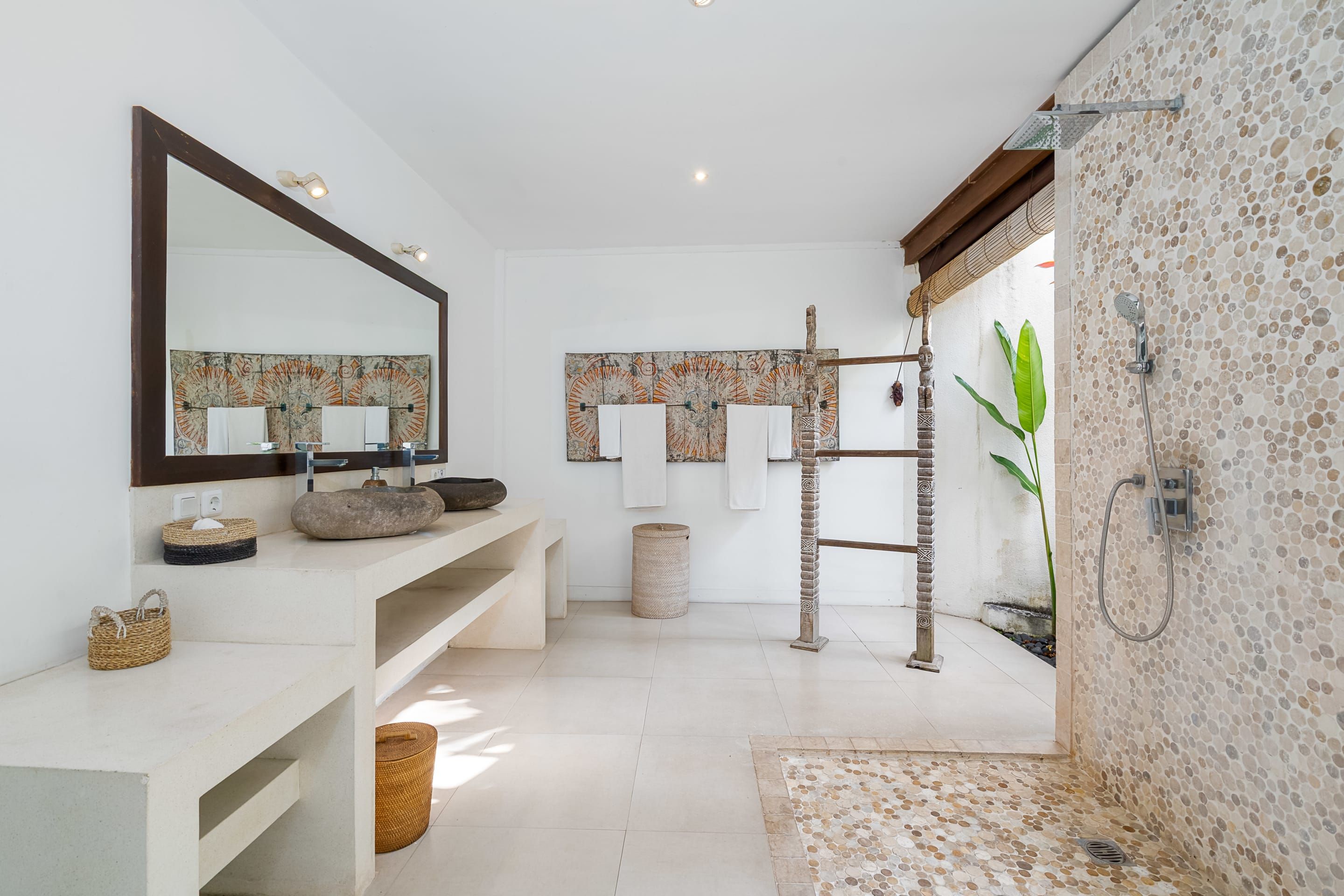 A modern bathroom with a large mirror, a stone sink, a shower with a mosaic wall, and a wooden ladder.