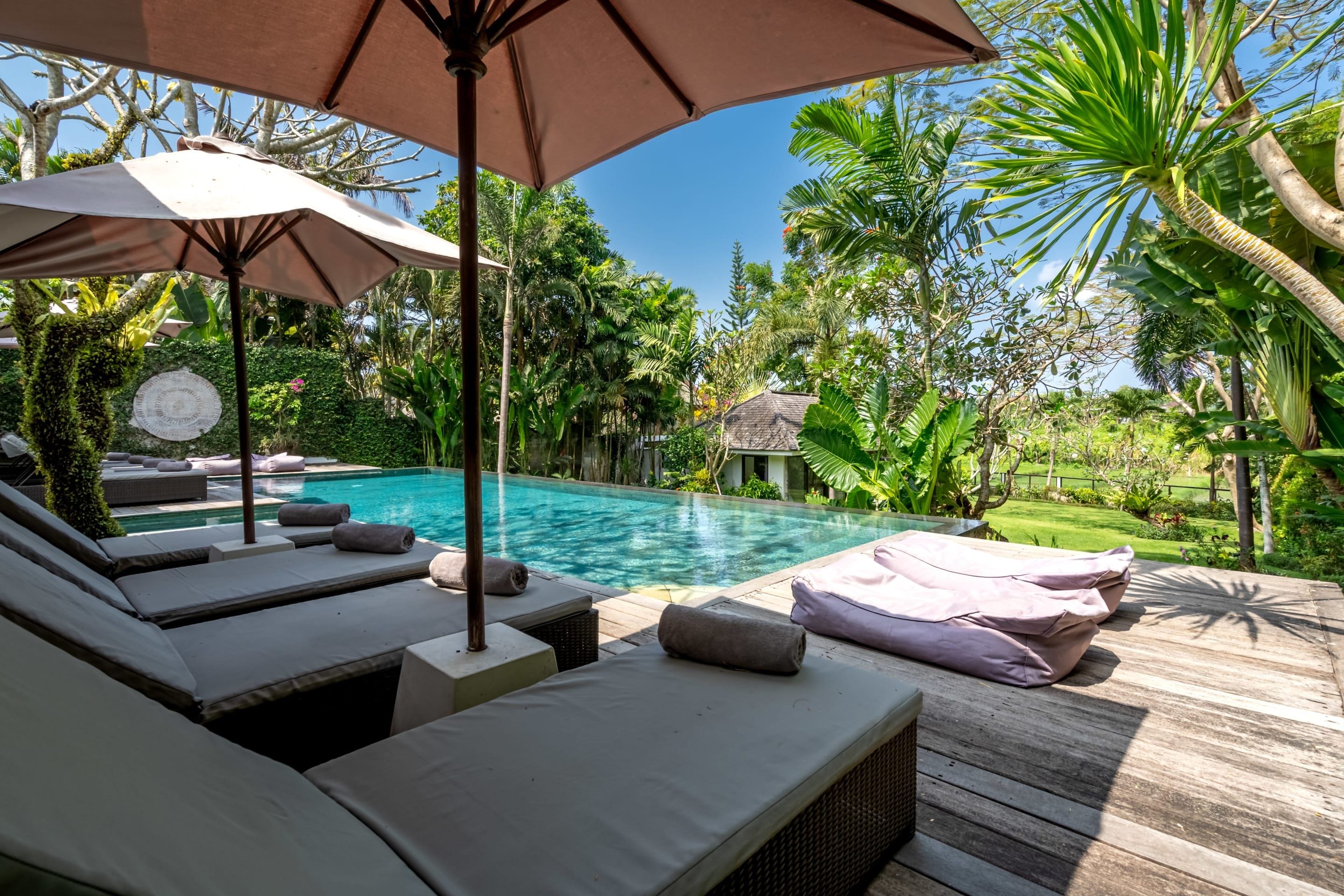 A poolside area with lounge chairs, a wooden deck, and a tropical garden.