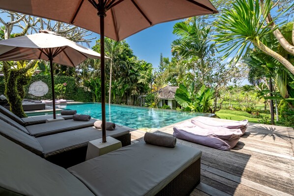 A poolside area with lounge chairs, a wooden deck, and a tropical garden.