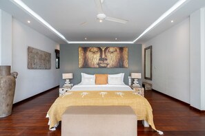 A modern bedroom with a large bed, two bedside tables with lamps, a ceiling fan, and artwork on the walls.