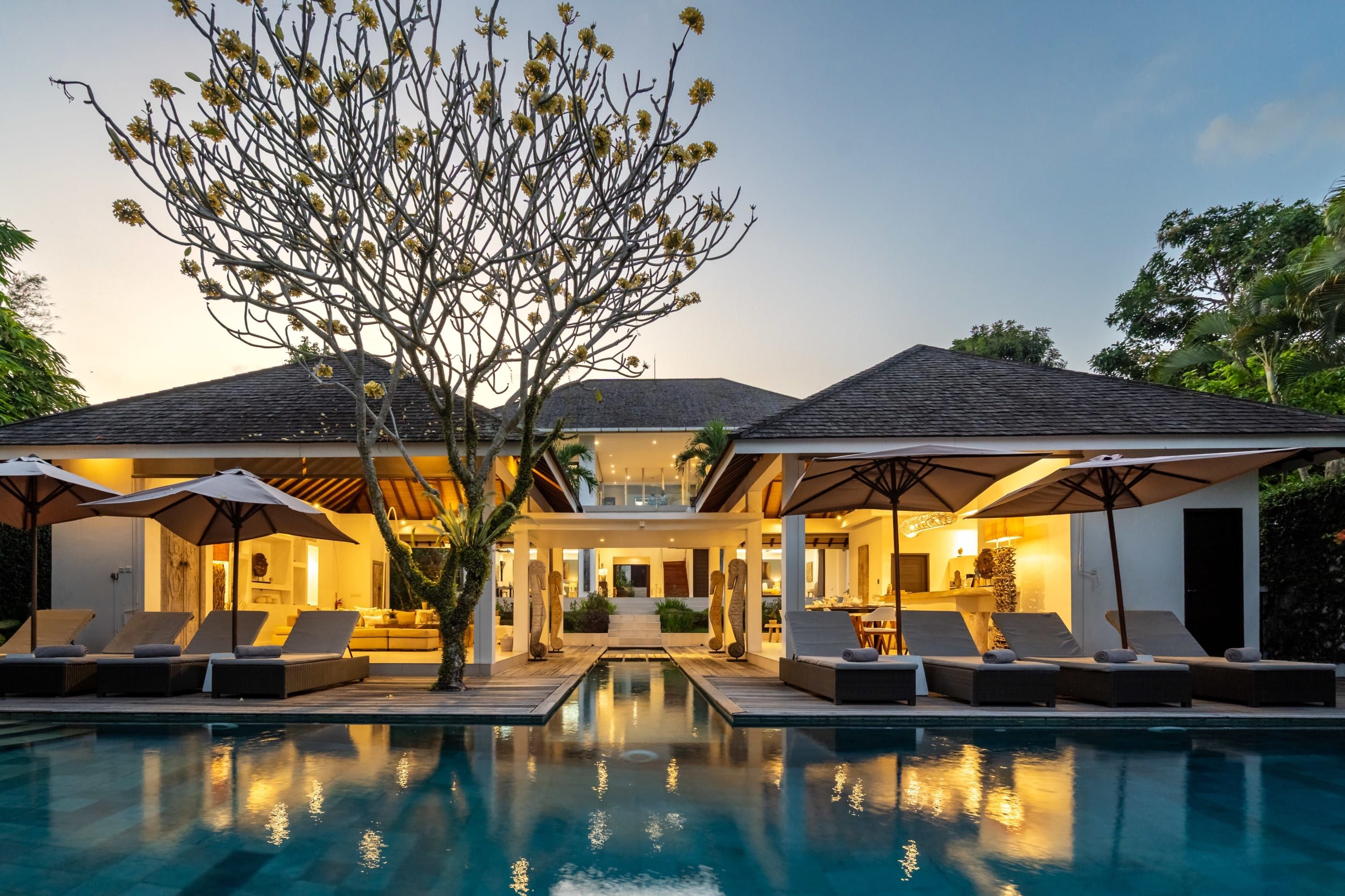 A modern house with a swimming pool, lounge chairs, and umbrellas.