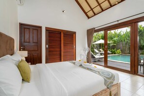A hotel room with a large bed, wooden doors, a view of a swimming pool, and a ceiling fan. - Villa Nolan (Canggu)