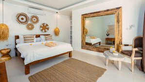 A modern bedroom with a large bed, a wooden chair, a small table, and decorative wall art. - Villa Marula (Seminyak)