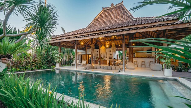 A poolside area with a covered seating area, a pool, and lush tropical plants. - Villa Marula (Seminyak)