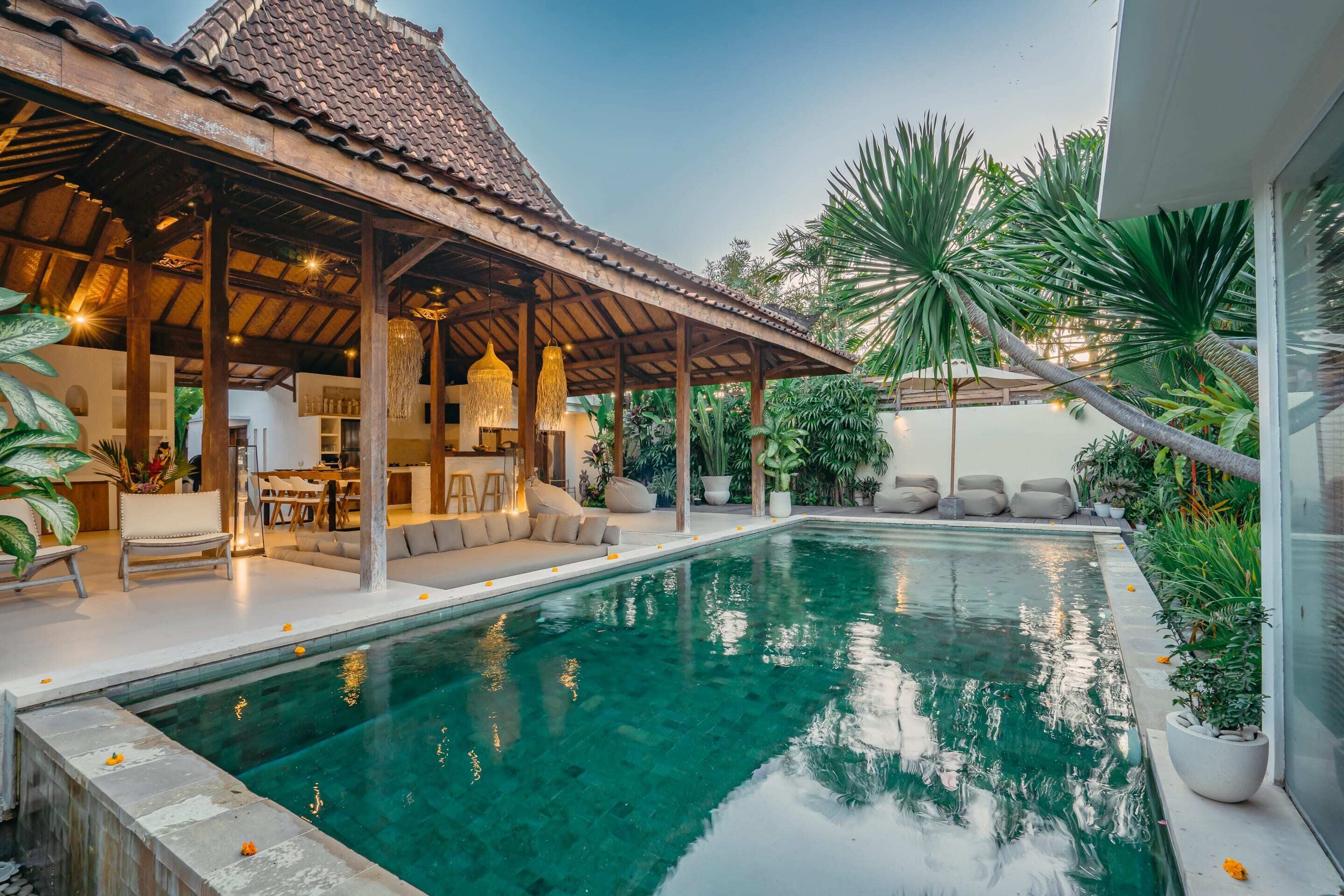 A poolside area with a covered seating area, a clear pool, and surrounding greenery.