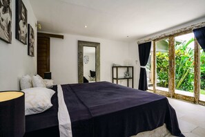 A bedroom with a bed, a nightstand, a mirror, and a window with curtains. - Villa Stella (Canggu)