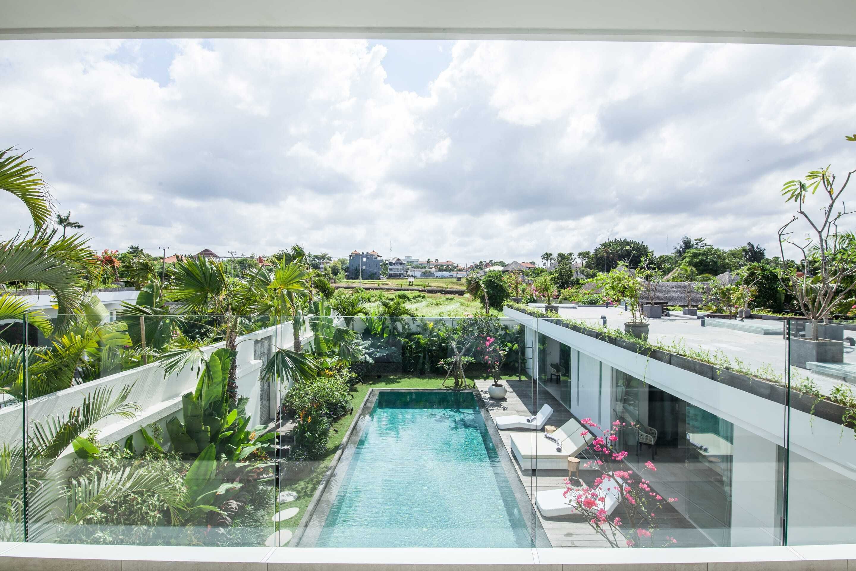 A modern pool area with glass railings, surrounded by lush greenery and a clear view of the cityscape in the background.