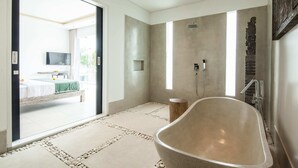 A modern bathroom with a freestanding bathtub, a shower, and a large window providing natural light. - Villa Clemence (Canggu)