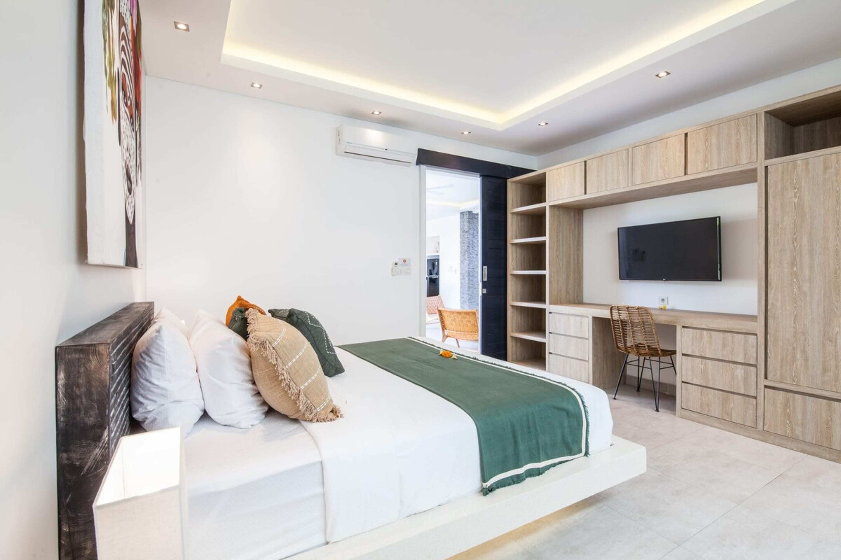 A modern bedroom with a bed, a desk, a chair, and a TV.