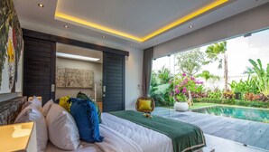 A modern bedroom with a large bed, a view of a swimming pool, and a balcony with lush greenery. - Villa Elisa (Canggu)