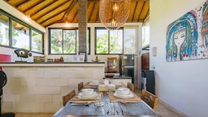 Un coin repas rustique avec une table en bois dressée pour quatre personnes, entourée de chaises, dans une pièce dotée d’un haut plafond en bois et de grandes fenêtres.