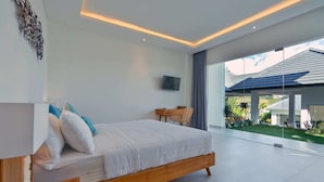 A modern bedroom with a large bed, a flat-screen TV, and a view of the outdoors. - Villa Ananda (Canggu)