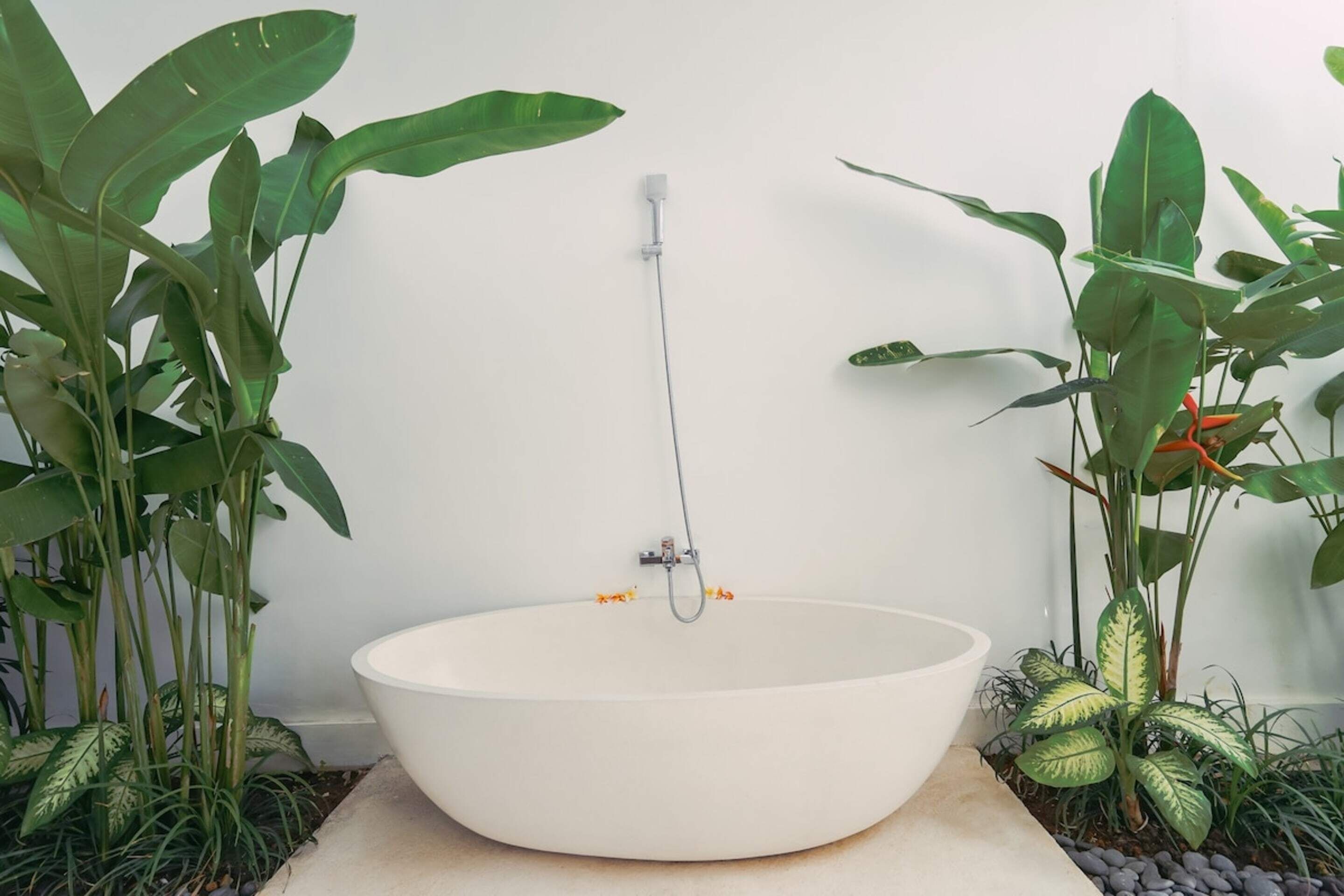 A large, white, freestanding bathtub in a corner with a showerhead attached to the wall.