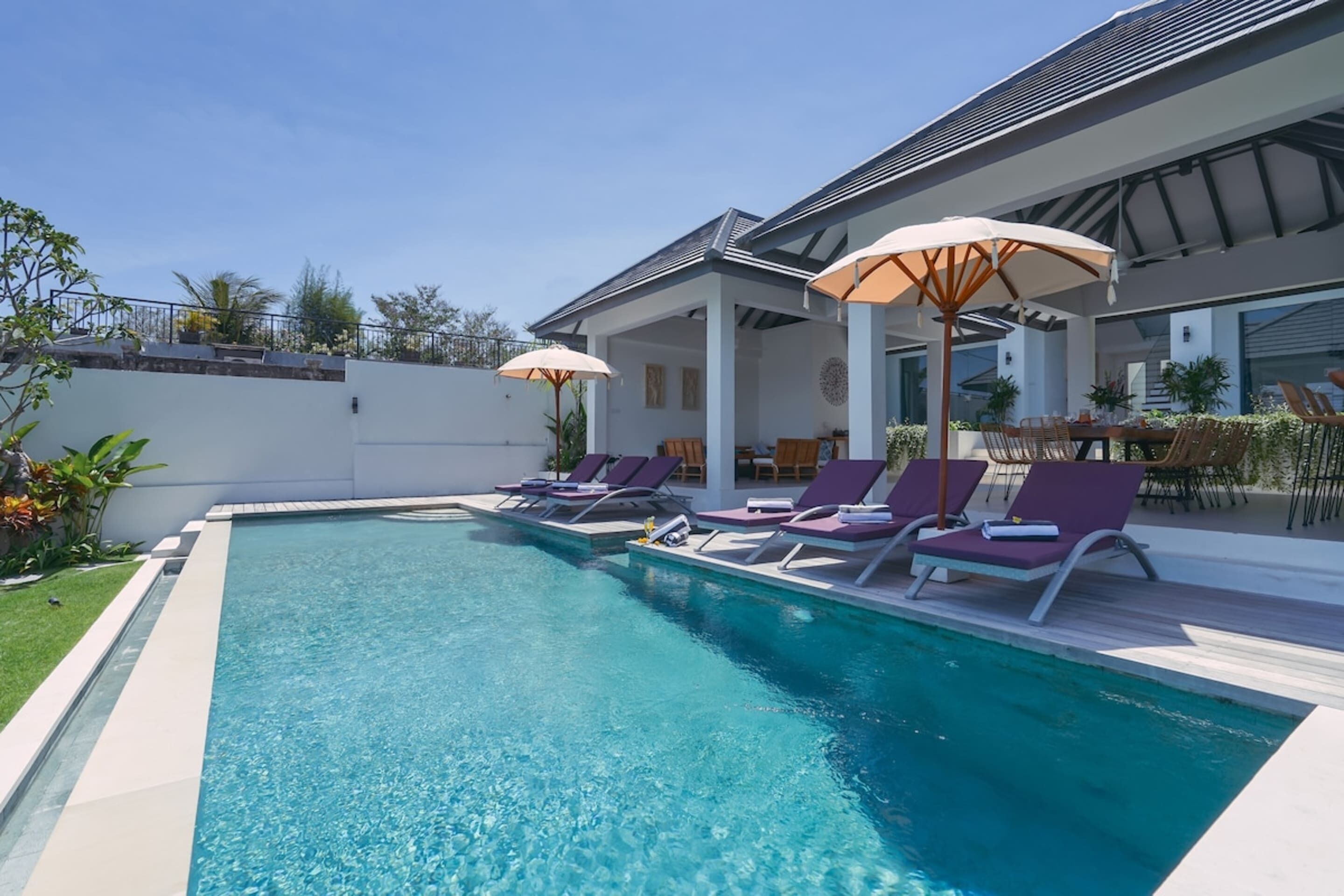 Ein Pool mit Liegestühlen und Sonnenschirmen, umgeben von einem modernen Gebäude mit großen Fenstern.