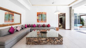 Una sala de estar moderna con una mesa baja de piedra, sofá gris con cojines de colores y pinturas abstractas en las paredes.