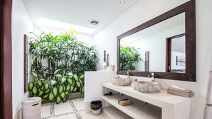 Un baño moderno con un espejo grande, lavamanos de piedra y un arreglo de plantas en macetas.