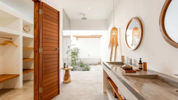 Un bagno moderno con un'ampia porta in legno, un mobile vanitario con specchio e una vasca da bagno visibile attraverso una porta aperta.