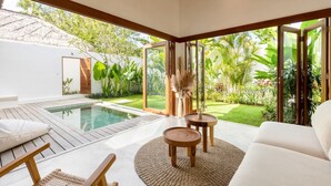 Un ambiente interno moderno con piscina, arredi in legno e ampie finestre che si affacciano su un giardino lussureggiante.