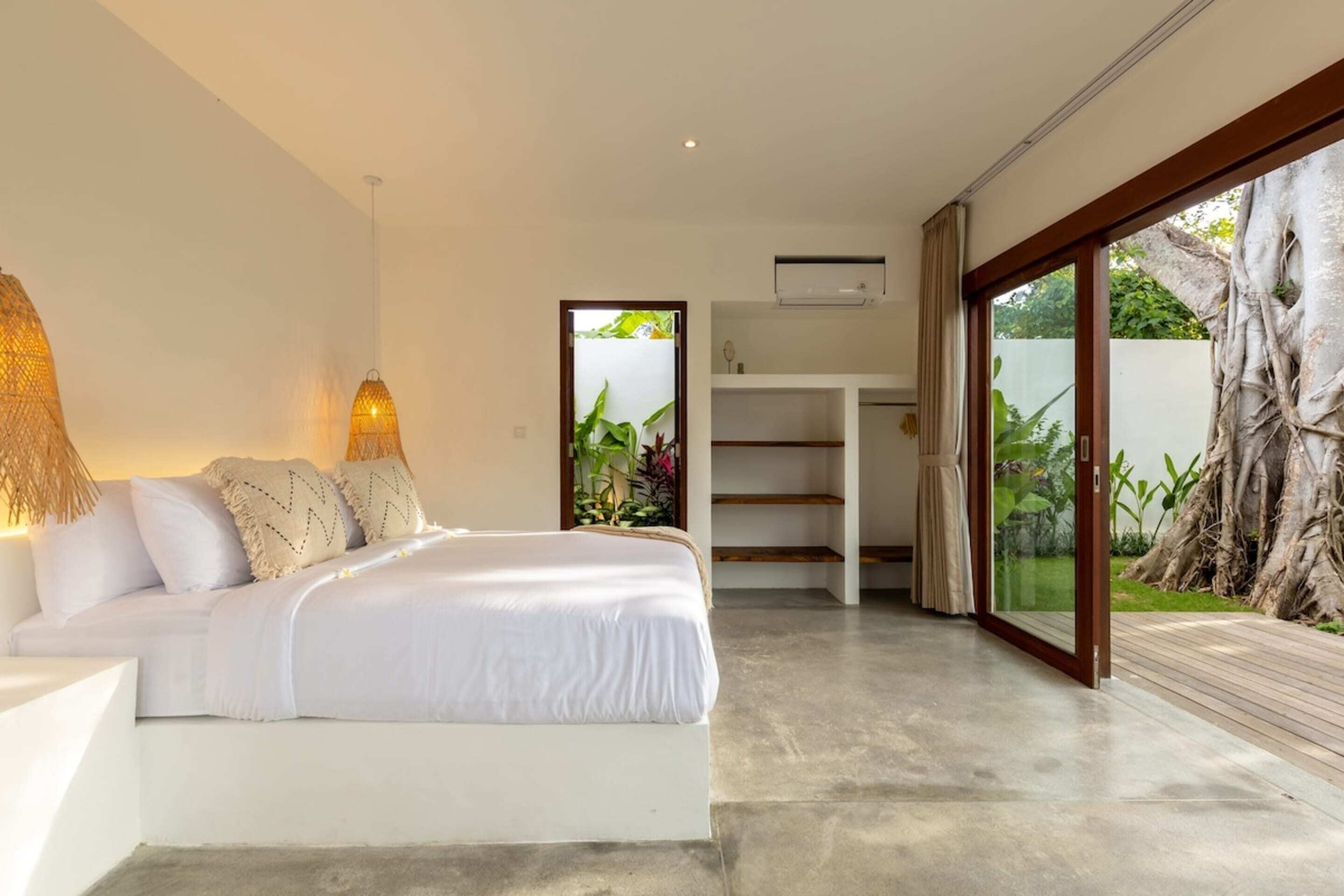 A modern bedroom with a large bed, bedside lamps, a built-in wardrobe, and a sliding glass door leading to a garden.