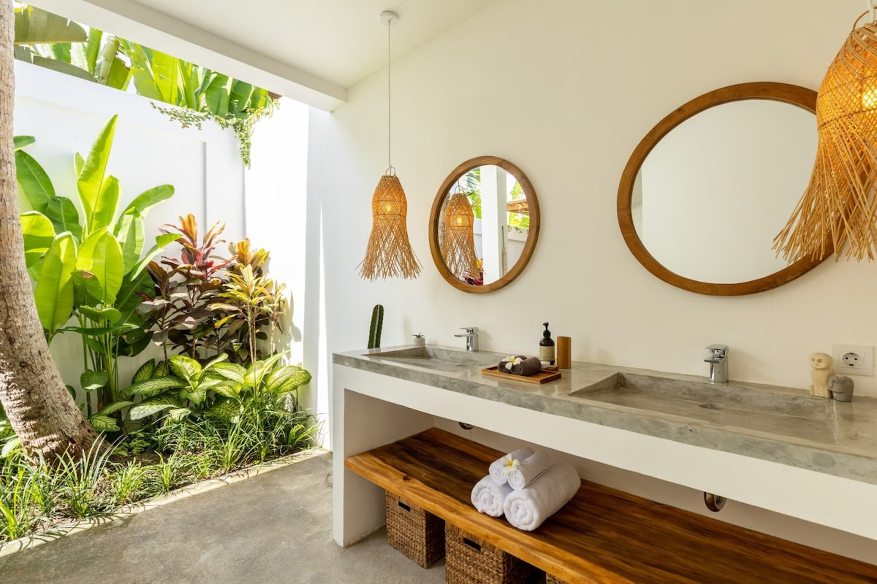 Une salle de bain avec un grand miroir, deux lampes suspendues, un lavabo et une étagère en bois où sont posées des serviettes.