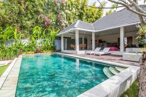 A swimming pool with a covered patio area, surrounded by lush greenery and a white fence. - Villa Imbuh 2 (Canggu)