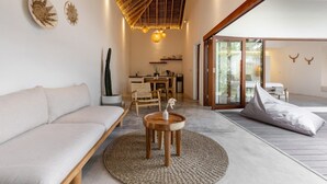 A modern living room with a sofa, a wooden coffee table, and a dining area with chairs and a table. - Villa Lumahi Dua (Cemagi)