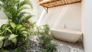 A modern bathroom with a freestanding bathtub, surrounded by lush greenery and a pebble pathway. - Villa Lumahi Dua (Cemagi)